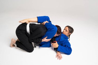 Jiu Jitsu kimonosu giyen iki kadın, beyaz bir stüdyonun arka planında prova yapıyorlar.