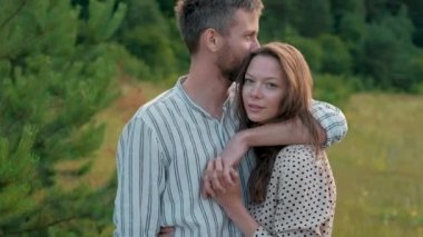Couple standing together outdoors, happy man hugging and kissing his wife