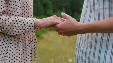 Man and woman holding by hands outdoors, young couple standing together in field