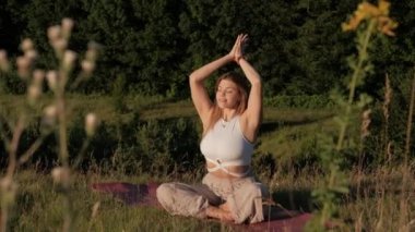 Young Woman Practicing Yoga and Meditation on the Mat Outdoors at Sunset with Beautiful Landscape on Background