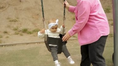 Mom swinging her little happy girl on the swing in the park, baby child on playground