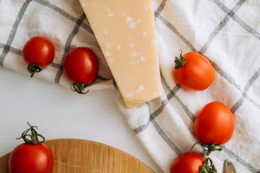Cherry tomatoes and a piece of parmesan cheese on the table with a kitchen towel and cutting board