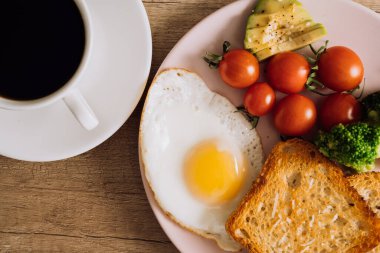 Close up homemade breakfast with cup of black coffee, fried egg and toast with tomatoes and avocado on plate
