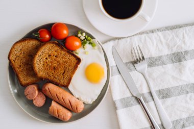 Breakfast plate with cup of black coffee, grilled sausage and whole wheat toast with fried egg and cherry tomatoes on plate