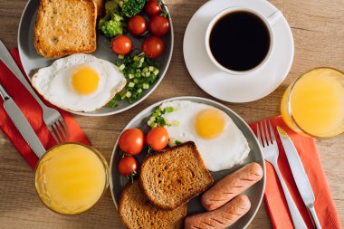 Flat lay of English breakfast with cup of black coffee and orange juice, grilled sausage and whole wheat toast with fried egg and cherry tomatoes