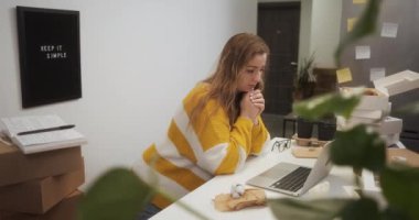 Entrepreneur female started her small business just in her apartment at home, woman works on a laptop in kitchen among boxes with goods