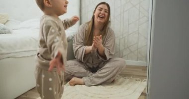 Little daughter dancing while young mother clapping hands next to her, happy mom and toddler having fun at home