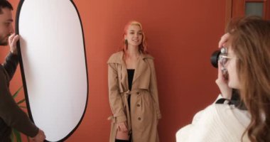 Process of photo session in the studio, female photographer with male assistant taking pictures of fashion model