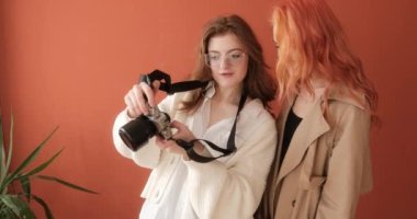 Female photographer shows the result of shoot to redhead model in the photo studio with terracotta background