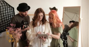 Photographer and assistant using tablet discussing results of shoot with model, teamwork in photo studio
