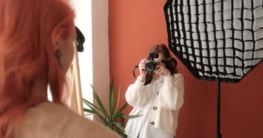 Kadın fotoğrafçı fotoğraf stüdyosunda kızıl saçlı bir mankenin fotoğraflarını çekiyor.