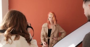 Red haired model at photo shoot in the studio, female photographer with assistant in the process of work