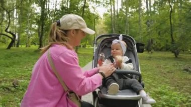  Mother in the park with her little daughter in baby carriage, mom playing with her child outdoors