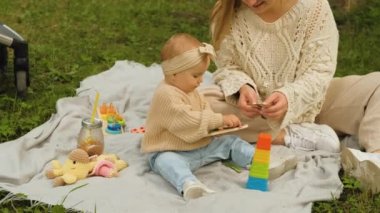 Anne, küçük kızıyla birlikte parkta piknikte çocuklara eğitim oyunları oynuyor, anne ve çocuk açık havada.