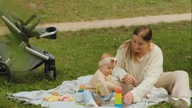 Mom with child outdoors, mother playing educational games for children with young baby daughter at a picnic in the park