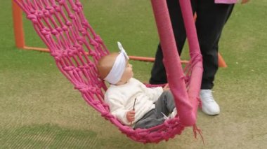 Little girl on a big swing, a mother rocking her child on a playground in the park. High quality 4k footage