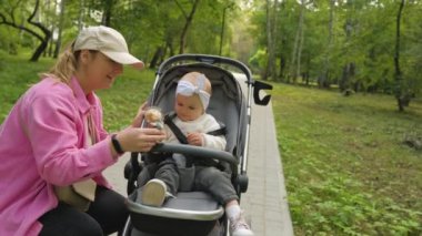  Mother in the park with her little daughter in a baby carriage, mom playing with her child outdoors. High quality 4k footage