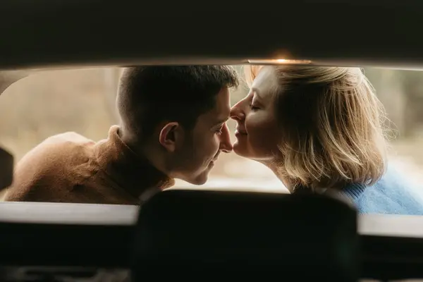 Intimate moment woman and man sitting in the open trunk of car while traveling in autumn and kissing