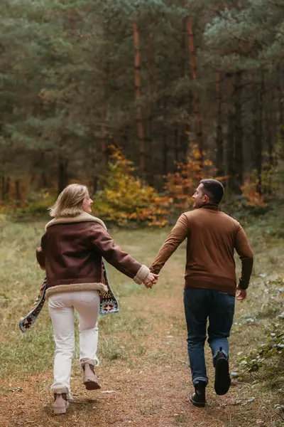在秋天的公园里 一对成年男女在一起玩的很开心 他们一边跑一边牵着手穿过树林 图库图片