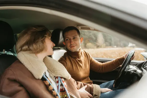Adult couple on a autumn road trip, a man and woman sitting in the car and looking on each other