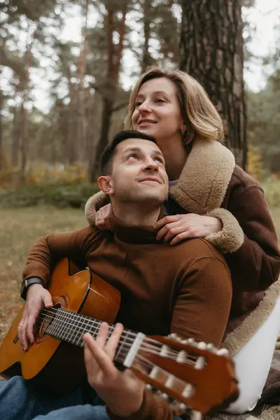 A man plays guitar and woman hugs him from behind in autumn park outdoors