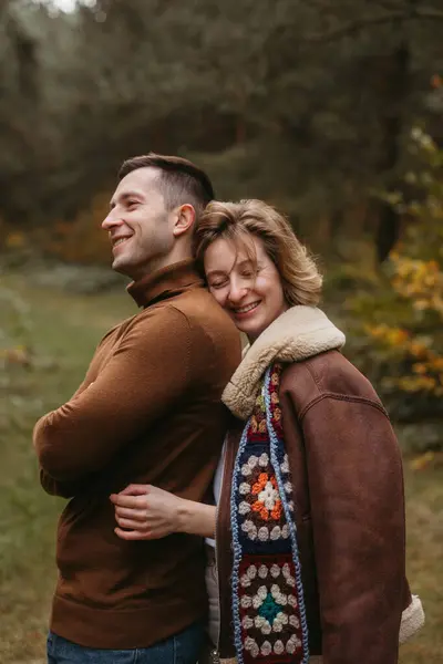 笑容可亲的高加索女人从背后拥抱着男人 快乐的夫妻在秋天的公园里呆着 图库图片