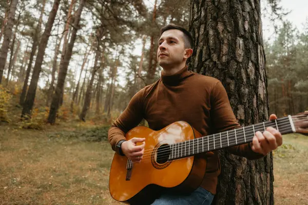 Hombre Caucásico Toca Guitarra Apoyado Árbol Bosque Rodeado Naturaleza Imagen de archivo