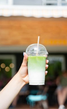 Elleri soğuk, buzlu, buzlu, buzlu latte ile plastik bardakta, ön kafe terasında saman tutan kadınlar. Yüksek kalite fotoğraf