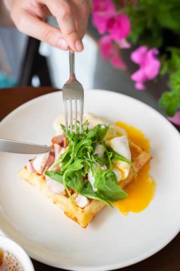 Pastırmalı haşlanmış yumurta tartışması ve elleri çatal bıçak tutan beyaz tabakta sos. Yüksek kalite fotoğraf