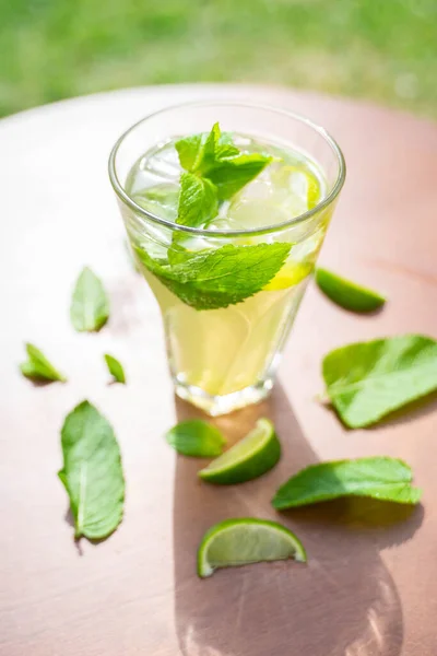 glass with fresh spring or summer iced drink mocktail with lemon and mint at table in caffe terrace in day light in front of trees and buildings. High quality photo