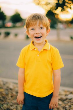 Günbatımı arka planında sarı gömlekli, gülümseyen, mutlu, genç bir çocuğun portresi. Yüksek kalite fotoğraf