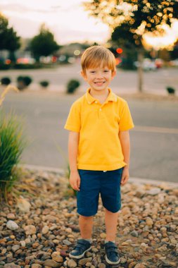 Günbatımı arka planında sarı gömlekli, gülümseyen, mutlu, genç bir çocuğun portresi. Yüksek kalite fotoğraf