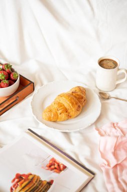 Beyaz tabakta Fransız hamur kruvasanı beyaz arka planda beyaz kahve ve çilekli yatak taklidi. Yüksek kalite fotoğraf