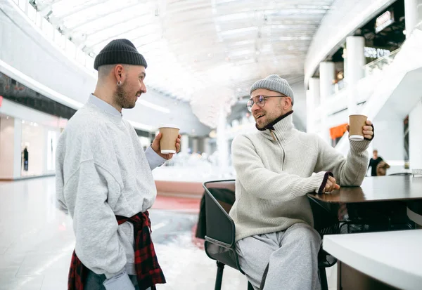 Barda ellerinde kahveyle şık giyinmiş iki genç adam.