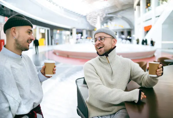 Beyaz kazaklı ve şapkalı iki genç bir kafede kahve içiyor..