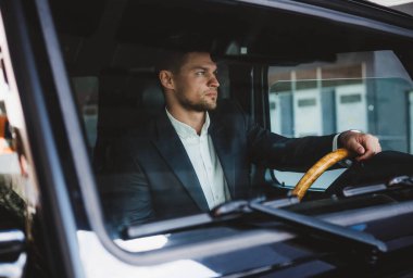 Yakışıklı genç işadamı lüks arabasını sürerken pencereden bakıyor.