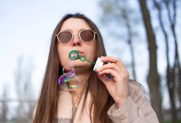 Genç bir kadın bir bahar günü dışarıda renkli sabun köpükleri üflüyor, neşeli ve rüya gibi bir anı yakalıyor.