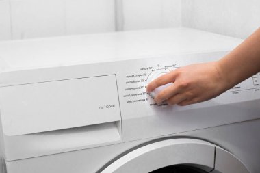 Kontrol kadranını çevirerek çamaşır makinesinin ayarlarını ayarlayan kişinin yakın çekim görüntüsü. Rahat ve günlük rutini temsil eden, temiz bir ev ortamında modern bir ev aleti.
