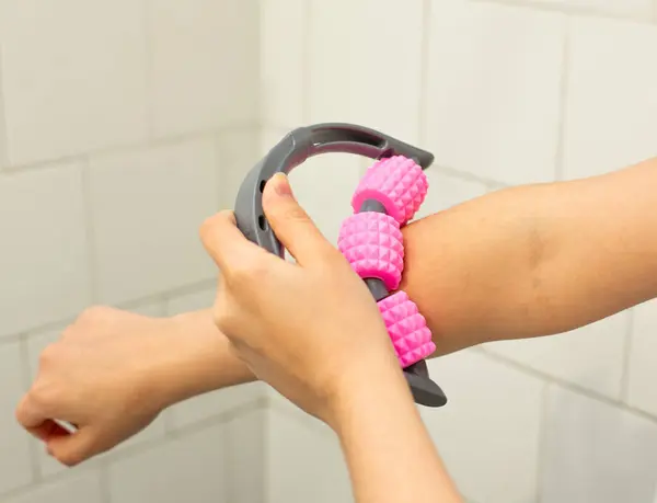 Kas gevşemesi ve kişisel bakım için üst koluna pembe masaj rulosu takan bir kadının yakın çekimi.