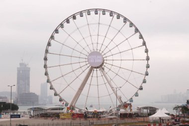 Merkez, Hong Kong - 30 Ocak 2016: Central Pier 'deki dönme dolap, Victoria Limanı ve Kowloon' daki gökdelenlerle birlikte bulutlu bir günde çekildi