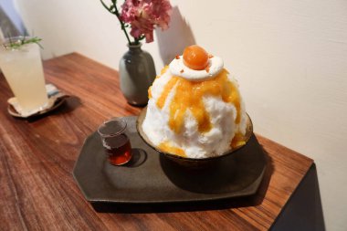 Geleneksel Japon Sobert soğuk tıraş edilmiş buzlu tatlı kakigori bingsu üzerine portakal reçeli sosu ve meyve, siyah tabakta oolong çayı sosu beyaz arka plan ve yaz aylarında ahşap masa.