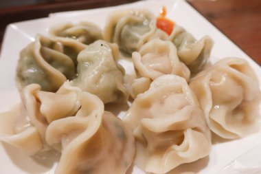 Çin buğulanmış haşlanmış et ve sebzeli domuz etli börekleri beyaz tabakta ve yanında baharatlı acı sosla birlikte.