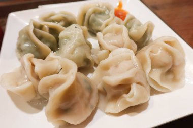 Çin buğulanmış haşlanmış et ve sebzeli domuz etli börekleri beyaz tabakta ve yanında baharatlı acı sosla birlikte.