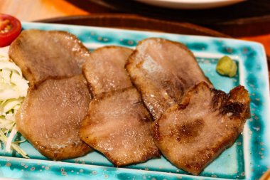 Yanında lahana ve vişneli domatesle kızartılmış yeşil tabakta Japon usulü ızgara sığır eti diliyle.