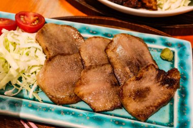 Yanında lahana ve vişneli domatesle kızartılmış yeşil tabakta Japon usulü ızgara sığır eti diliyle.