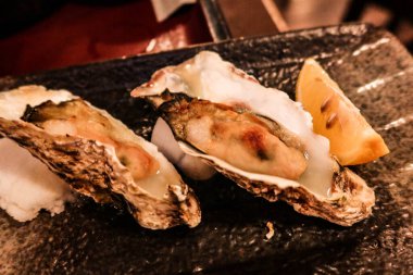 Siyah tabakta iki çiğ istiridye ve yanında limon dilimi.