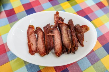 close up of Chinese Cantonese barbecued grilled Char Siu pork on a white plate with colourful table cloth clipart