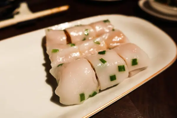 stock image close up of steamed rice roll with shrimp deep fried crispy spring roll and prawns cut into nine pieces with spring onion as toppings on a white plate