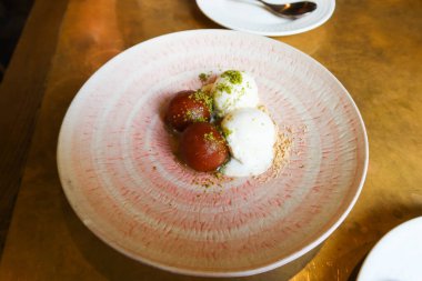 Geleneksel Hint tatlılarından Gulab Jamun 'a yakın pembe ve beyaz tabakta vanilyalı dondurma.
