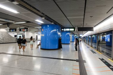 Deniz Kuvvetleri, Hong Kong - 28 Ağustos 2024: Mtr tren istasyonu peronunda cam ön pencere pervazı ile Tsuen Wan Hattı demiryolu reklam panosu ile bekleyen ve yürüyen yolcular